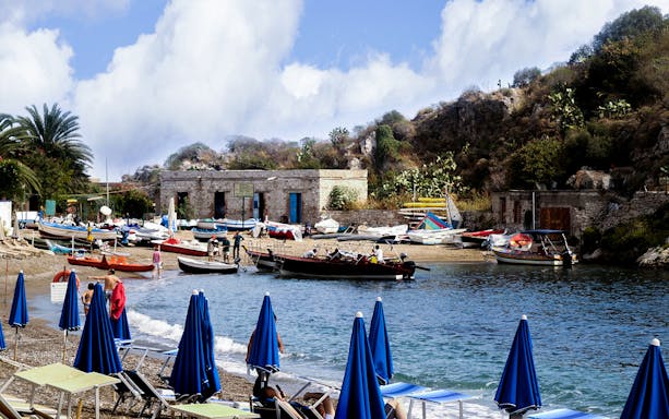 Excursion boats docked at Giardini Naxos beach near Taormina, with Isola Bella in the background.