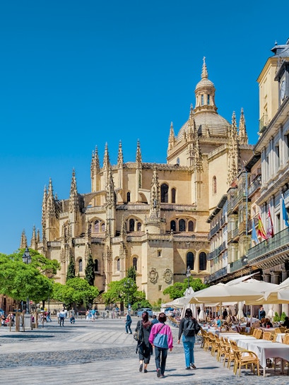 Segovia Cathedral in Plaza Mayor with people walking and outdoor cafes.