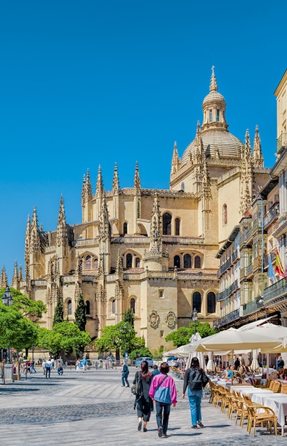 Segovia Cathedral in Plaza Mayor with people walking and outdoor cafes.