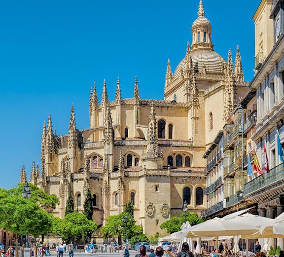 Segovia Cathedral in Plaza Mayor with people walking and outdoor cafes.