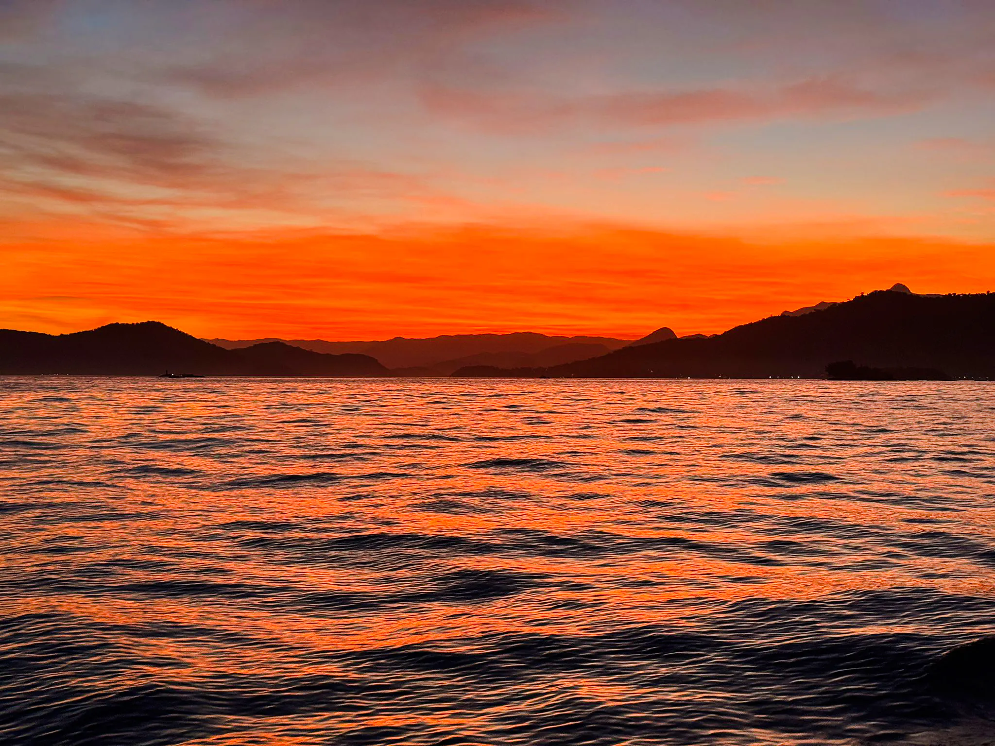 Sunset over the ocean with silhouetted mountains in Arraial do Cabo, Brazil.