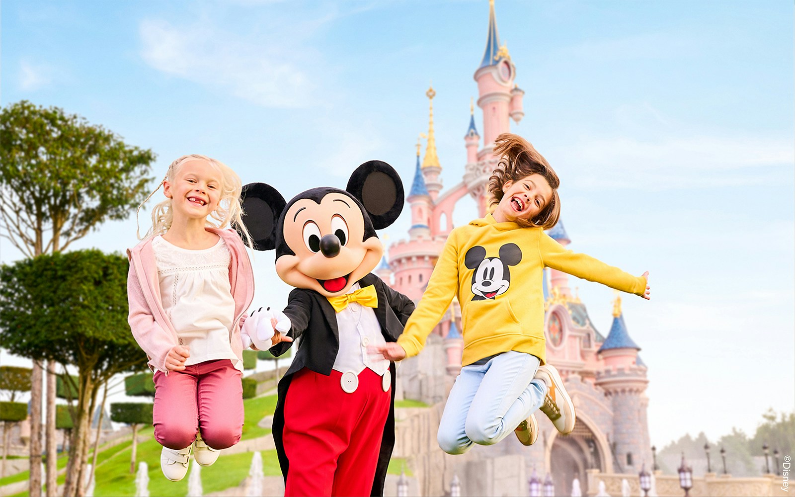 Mickey Mouse with children jumping in front of Sleeping Beauty Castle at Disneyland Paris.