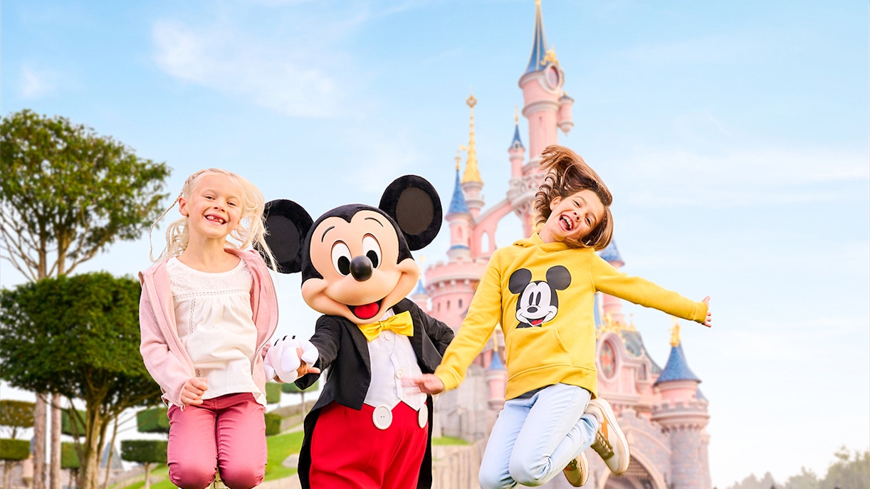 Mickey Mouse with children jumping in front of Sleeping Beauty Castle at Disneyland Paris.