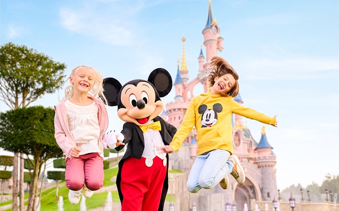 Mickey Mouse with children jumping in front of Sleeping Beauty Castle at Disneyland Paris.