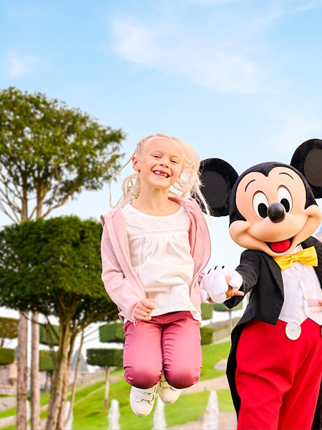 Mickey Mouse with children jumping in front of Sleeping Beauty Castle at Disneyland Paris.