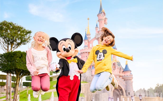 Mickey Mouse with children jumping in front of Sleeping Beauty Castle at Disneyland Paris.