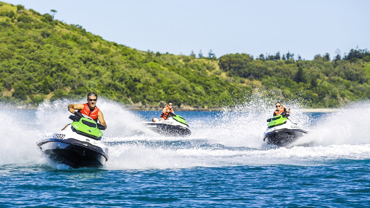 Tourists riding jetskis in the Whitsundays with lush green hills in the background.