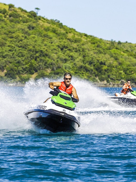 Tourists riding jetskis in the Whitsundays with lush green hills in the background.