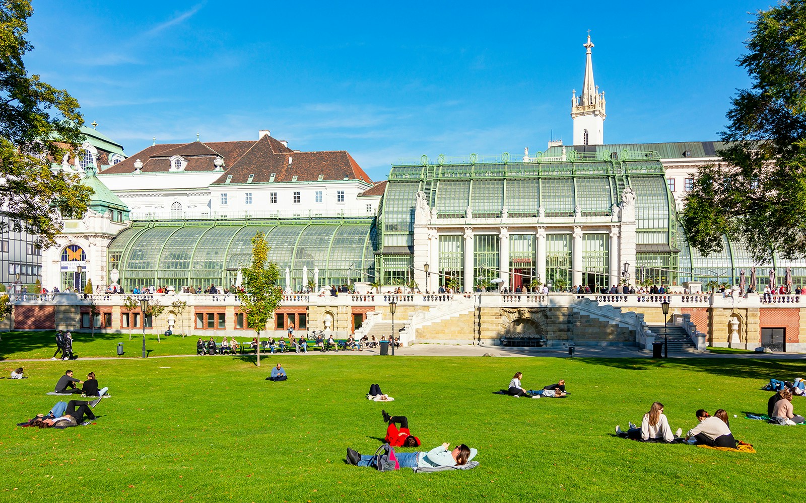 People relaxing on the lawn in front of the Palm House at Schönbrunn Palace Zoo, Vienna.