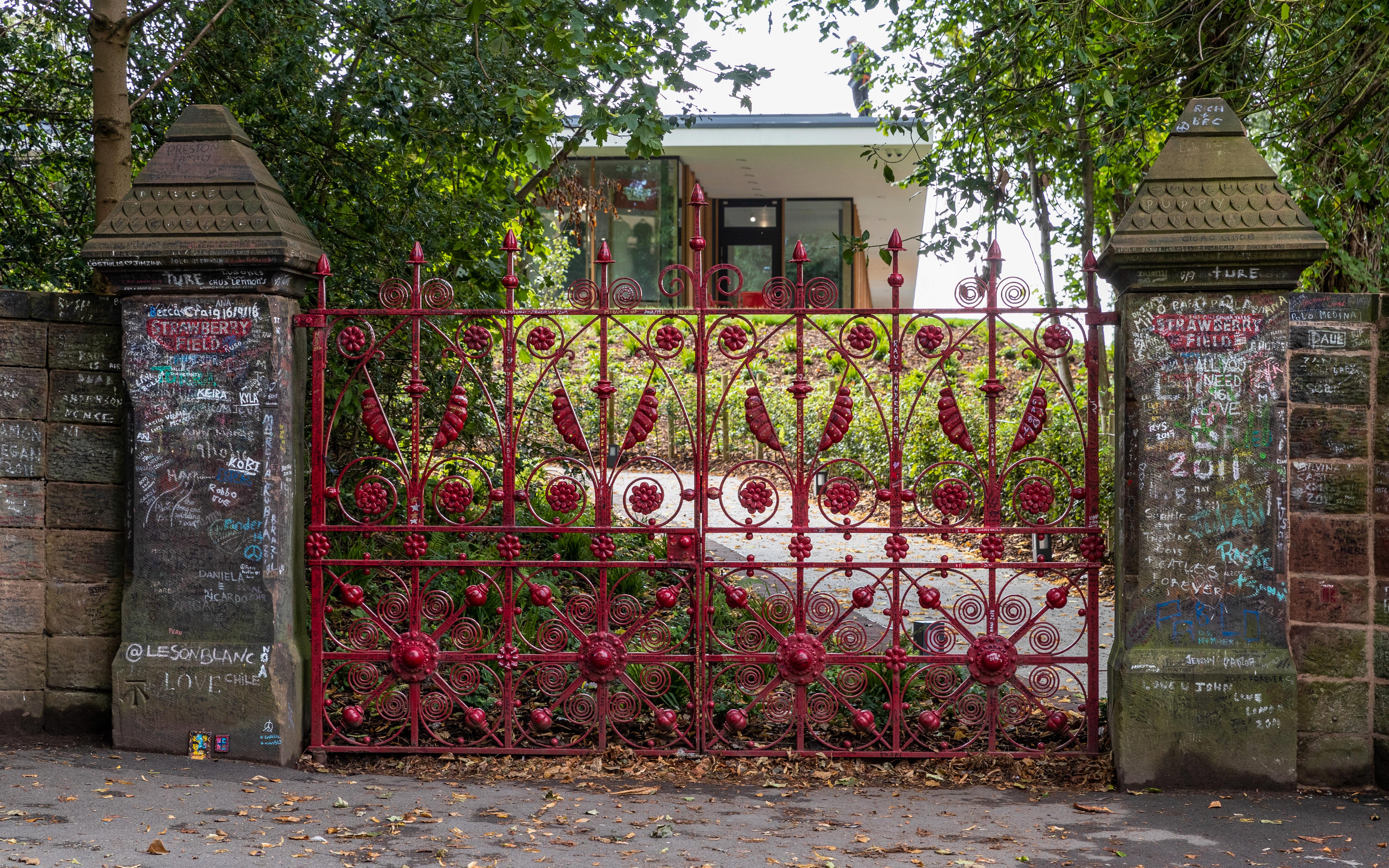 Red ornate gate at Strawberry Fields entrance, Liverpool, with graffiti-covered stone pillars.