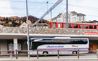 Bernina Red Train passing through St. Moritz station with a tour bus parked below.