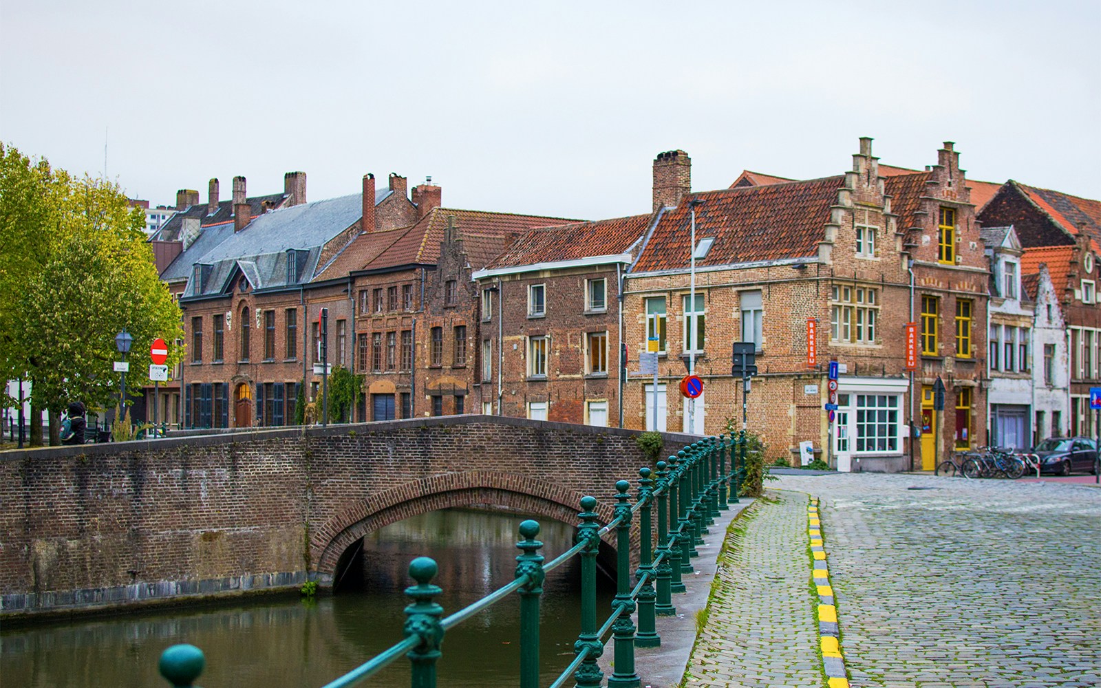 Patershol street with brick buildings, green railings, and Lys river bridge in Belgium.