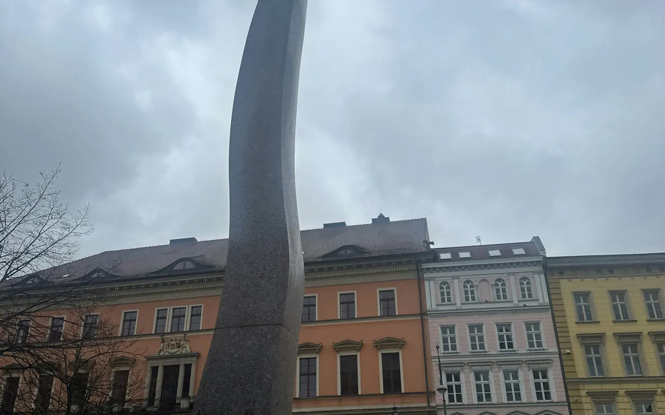 Curved monument in front of colorful historic buildings in Wroclaw's Old Town.