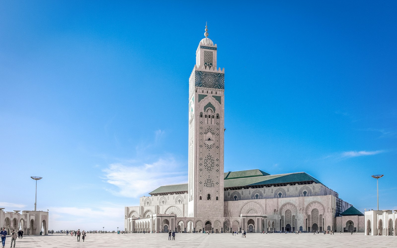 Tourists exploring the magnificent Hassan II Mosque in Casablanca, Morocco, with its towering minaret and intricate architecture