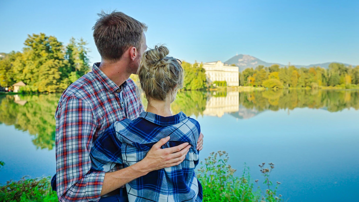 Couple admiring Leopoldskron Palace across the lake in Salzburg, Austria.