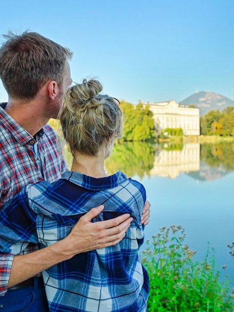 Couple admiring Leopoldskron Palace across the lake in Salzburg, Austria.