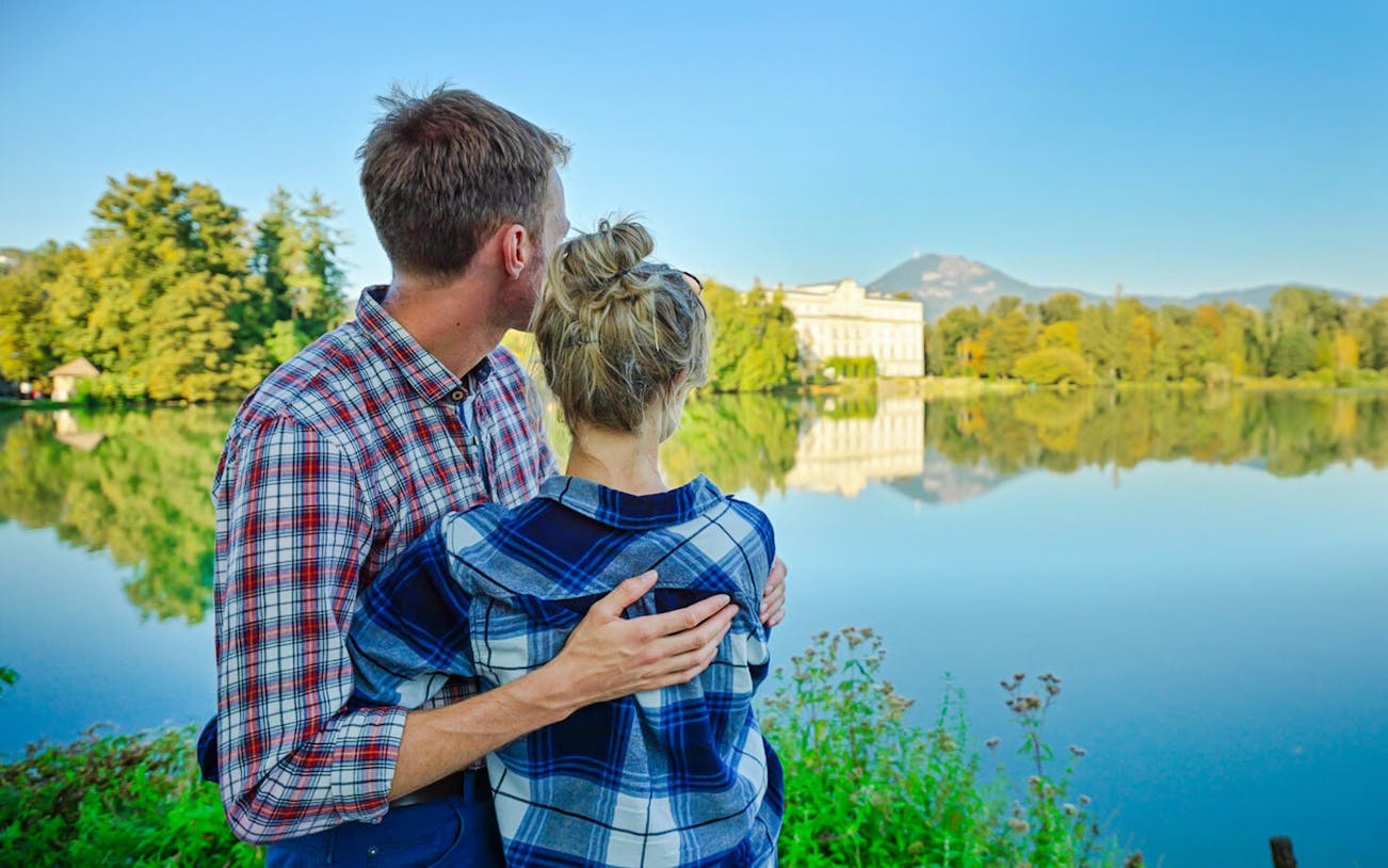 Couple admiring Leopoldskron Palace across the lake in Salzburg, Austria.