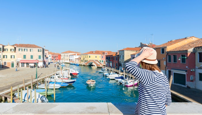 Traveler admiring Murano Island canal with colorful buildings near Venice, Italy.