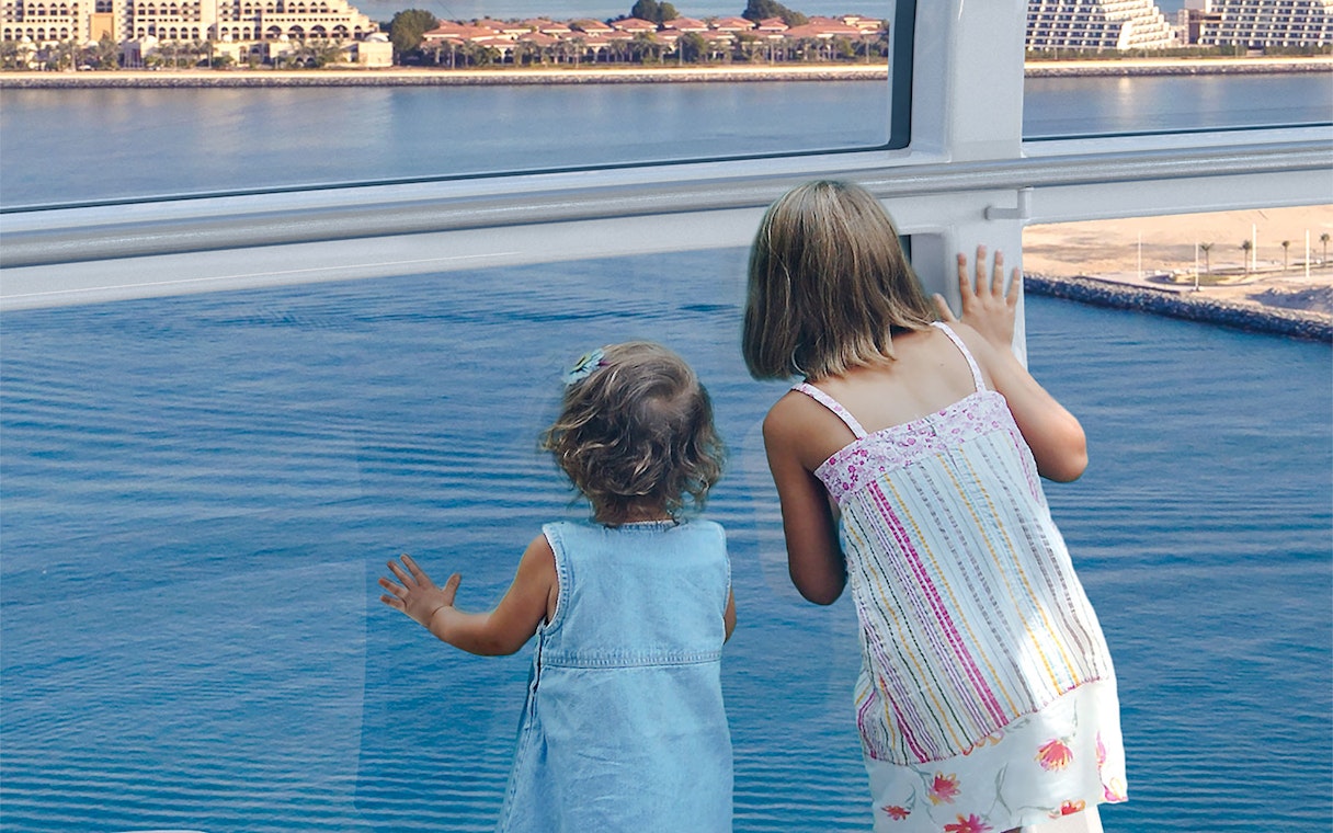 Children looking out from Ain Dubai wheel at waterfront view.
