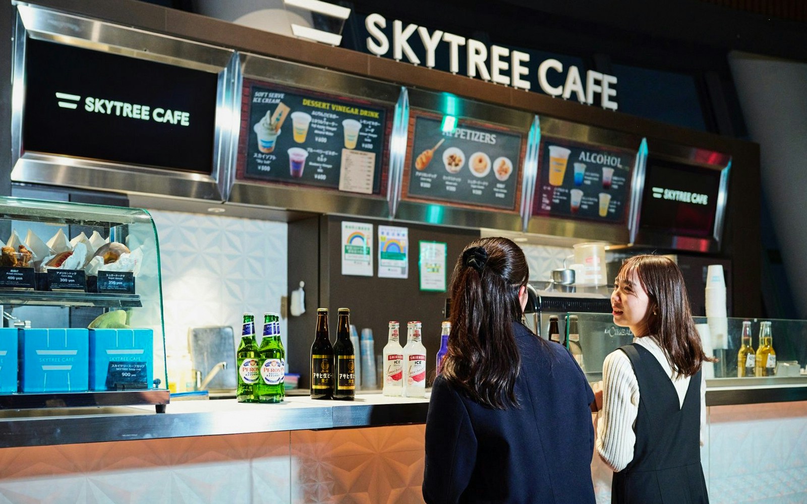 Tourists enjoying drinks at Skytree Cafe on Tokyo's Tembo Deck with city skyline views.