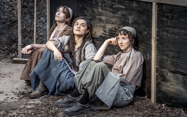 Three actors in period costumes sitting against a wooden wall, scene from Fiddler on the Roof.