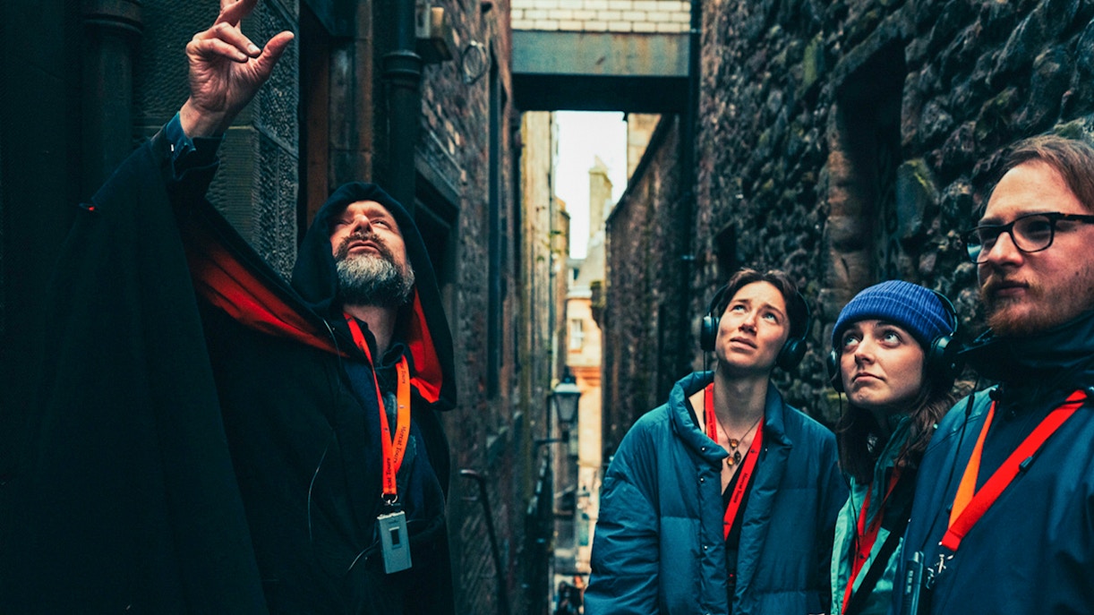Guide leading a late-night walking tour in Edinburgh alley with attentive group.