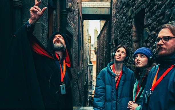 Guide leading a late-night walking tour in Edinburgh alley with attentive group.