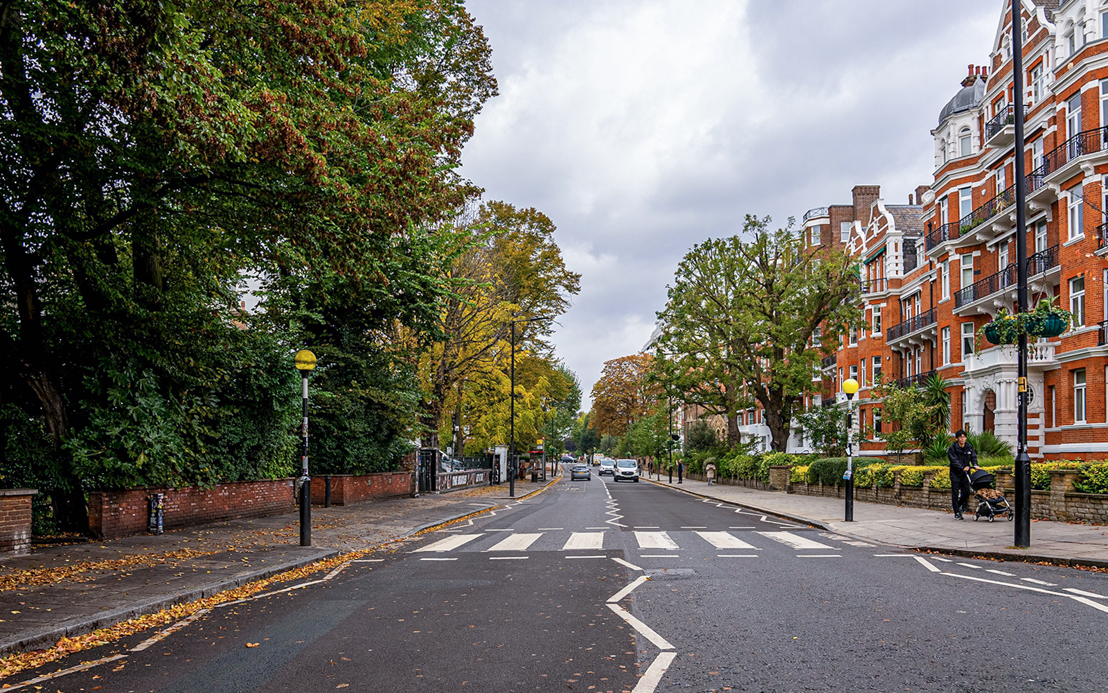 Abbey Road zebra crossing in London with red brick buildings and trees lining the street.