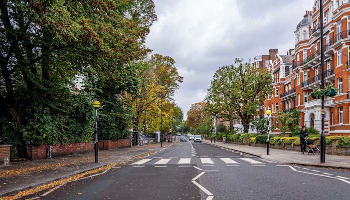 Abbey Road zebra crossing in London with red brick buildings and trees lining the street.