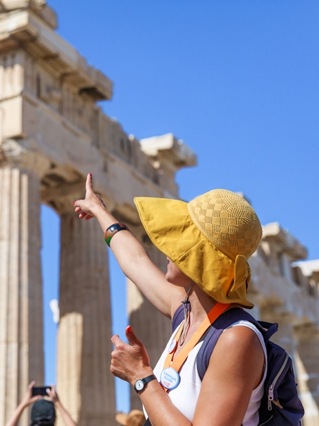Tourists exploring the Acropolis with a guide pointing at the Parthenon in Athens.