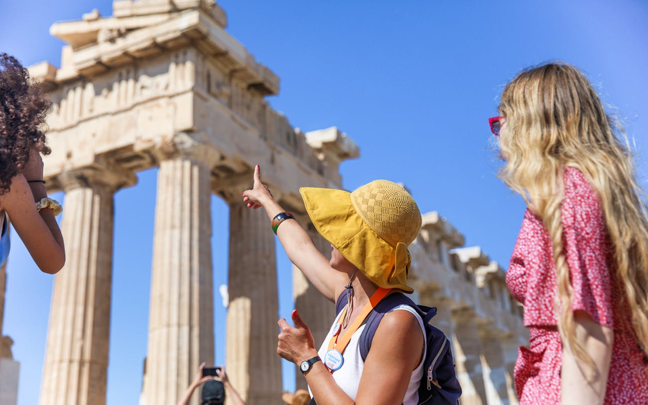 Tourists exploring the Acropolis with a guide pointing at the Parthenon in Athens.