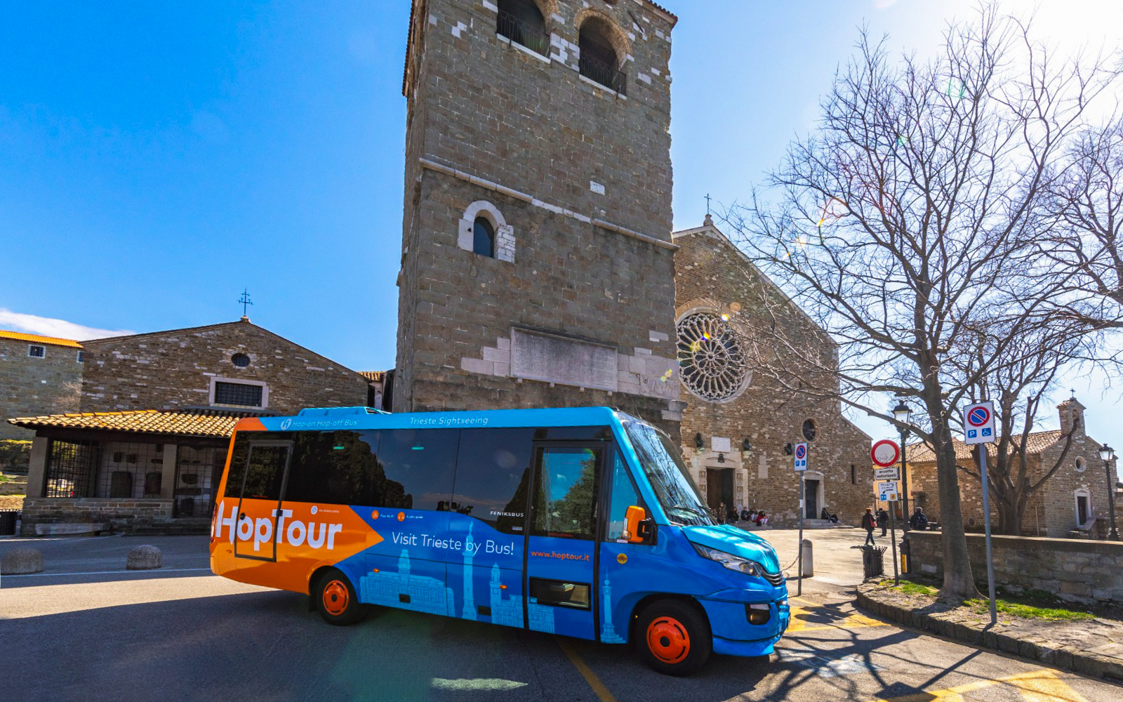 Hop-on hop-off bus in front of historic church in Trieste, Italy.