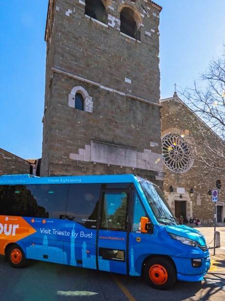 Hop-on hop-off bus in front of historic church in Trieste, Italy.