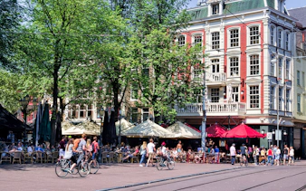 Bicyclists and people at outdoor cafes in Amsterdam's Leidseplein.