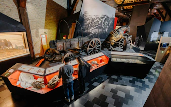 Museum visitors view WWI artifacts and exhibits, including a horse-drawn cart, on the Flanders Fields tour.