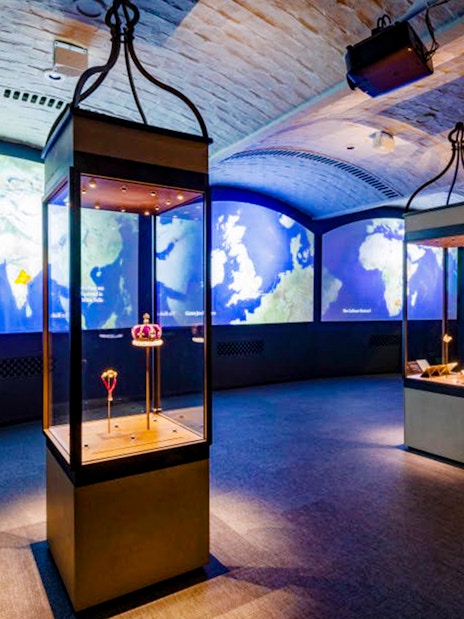 Exhibit room with illuminated display cases and world maps at Historic Royal Palaces.