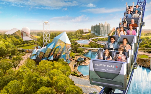 Roller coaster at Futuroscope with excited riders, futuristic architecture in background.