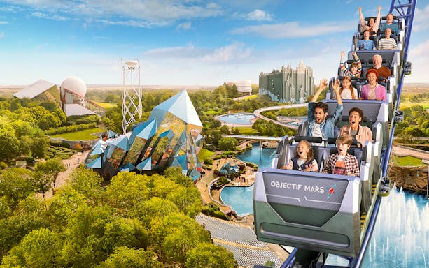 Roller coaster at Futuroscope with excited riders, futuristic architecture in background.