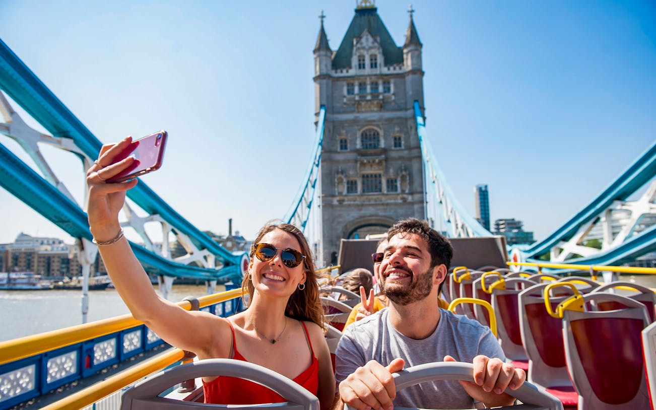 Tourists taking a selfie on a Tootbus in front of Tower Bridge, London.