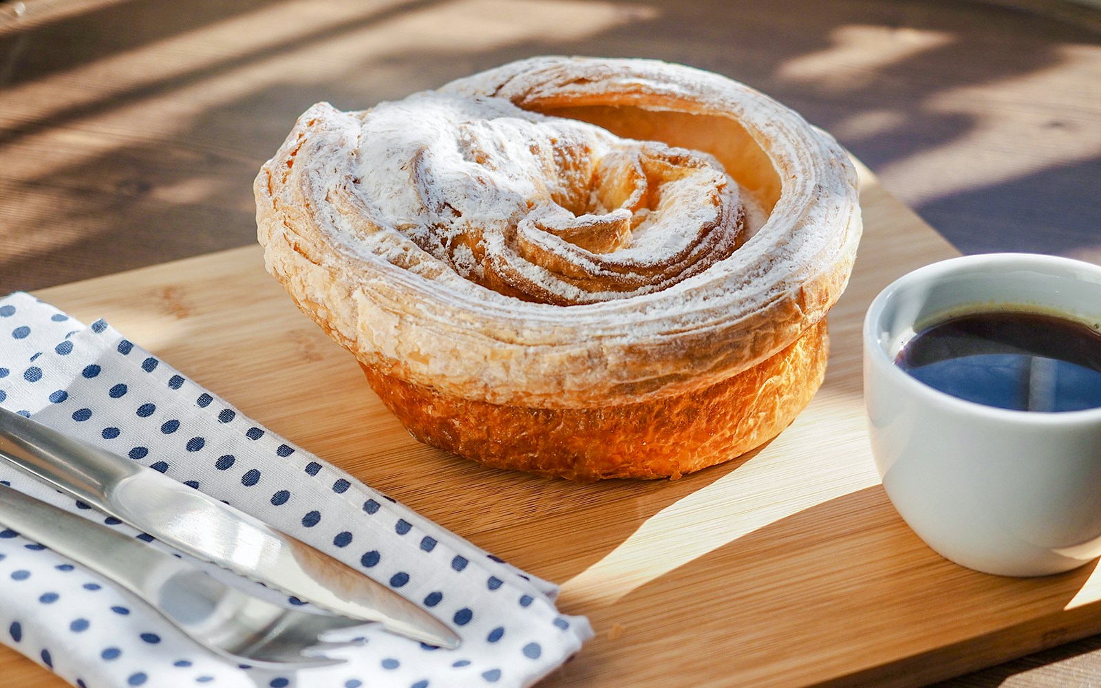 Pastry with powdered sugar and a cup of coffee on a wooden board.