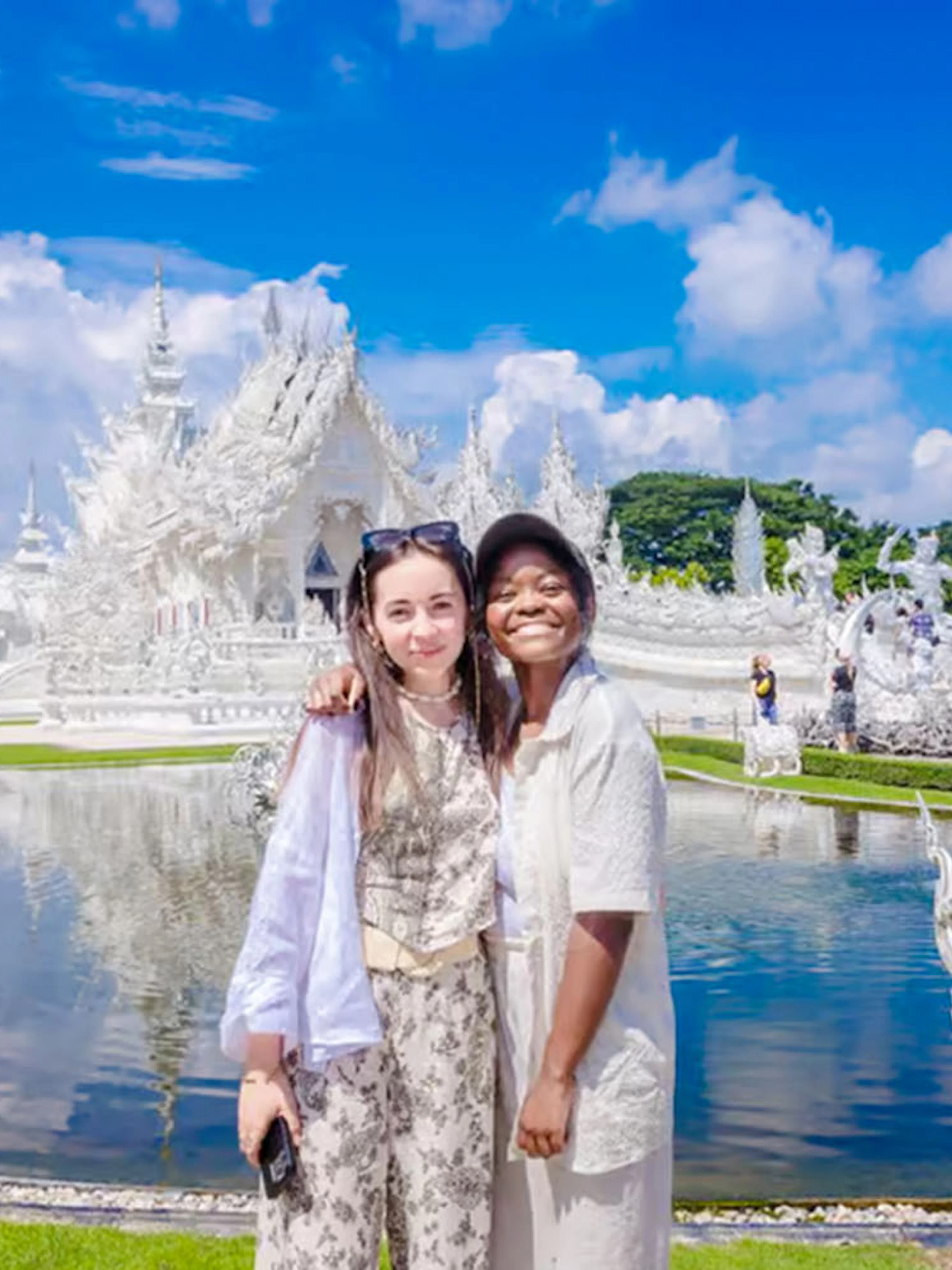 Tourists smiling in front of Wat Rong Khun temple in Thailand.