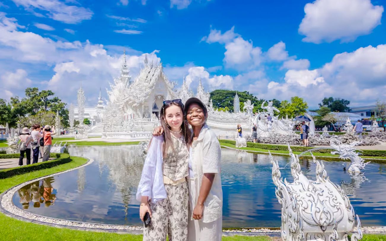 Tourists smiling in front of Wat Rong Khun temple in Thailand.