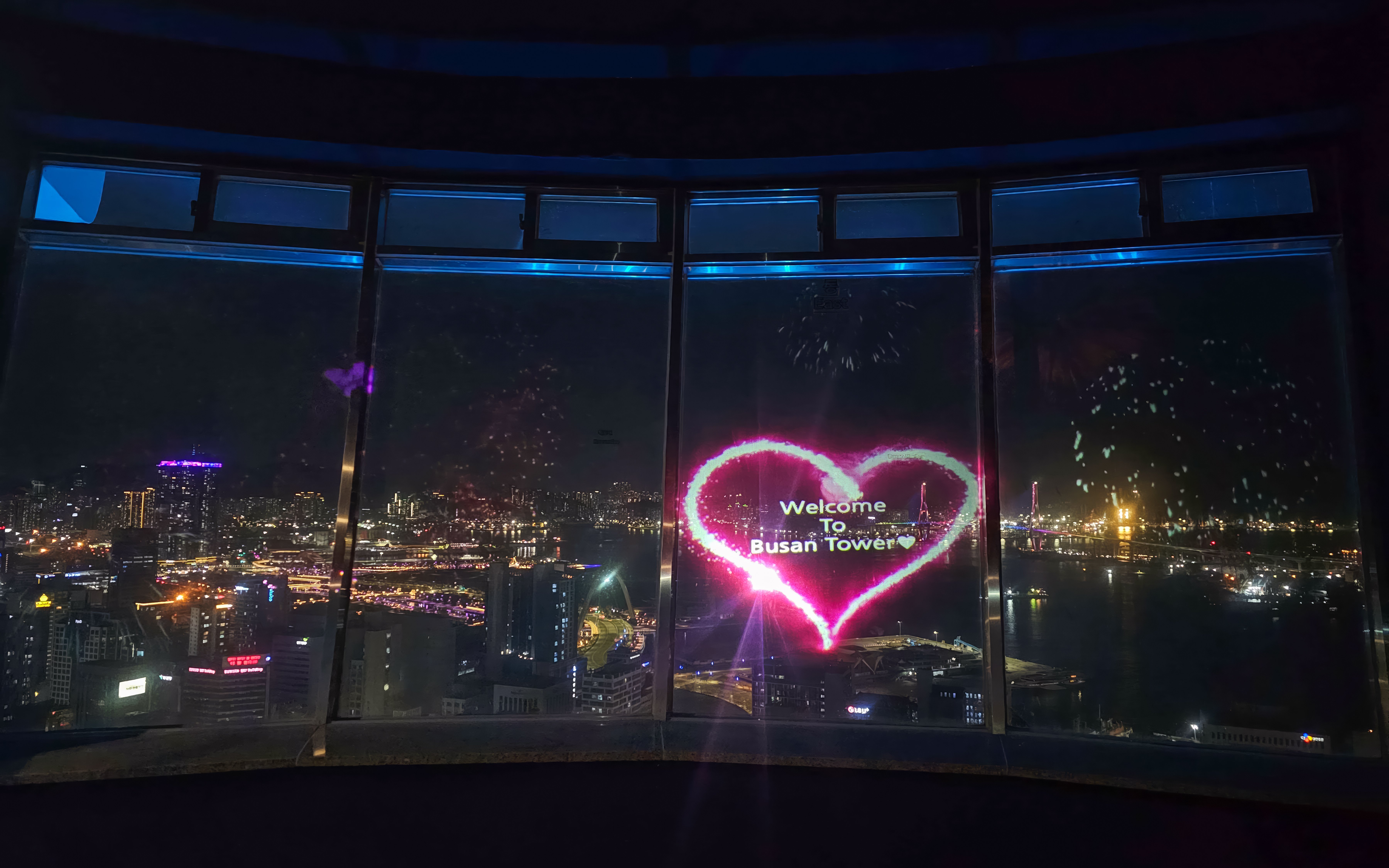 Busan Tower observatory view with city lights and heart-shaped welcome sign.