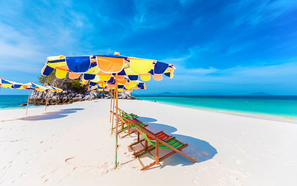 Colorful beach umbrellas and chairs on a sandy shore, Khai Island, Phuket tour.
