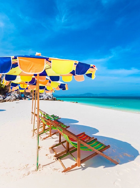 Colorful beach umbrellas and chairs on a sandy shore, Khai Island, Phuket tour.