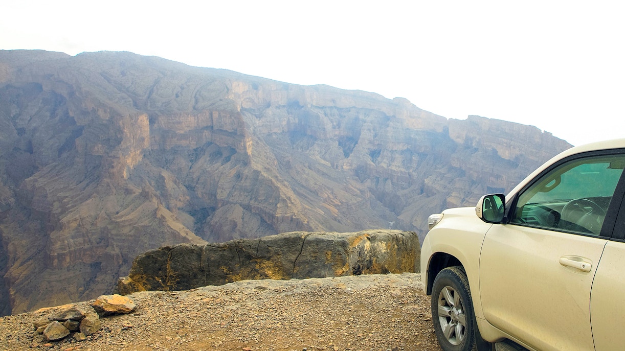4x4 vehicle parked on a mountain edge with rocky cliffs in the background.