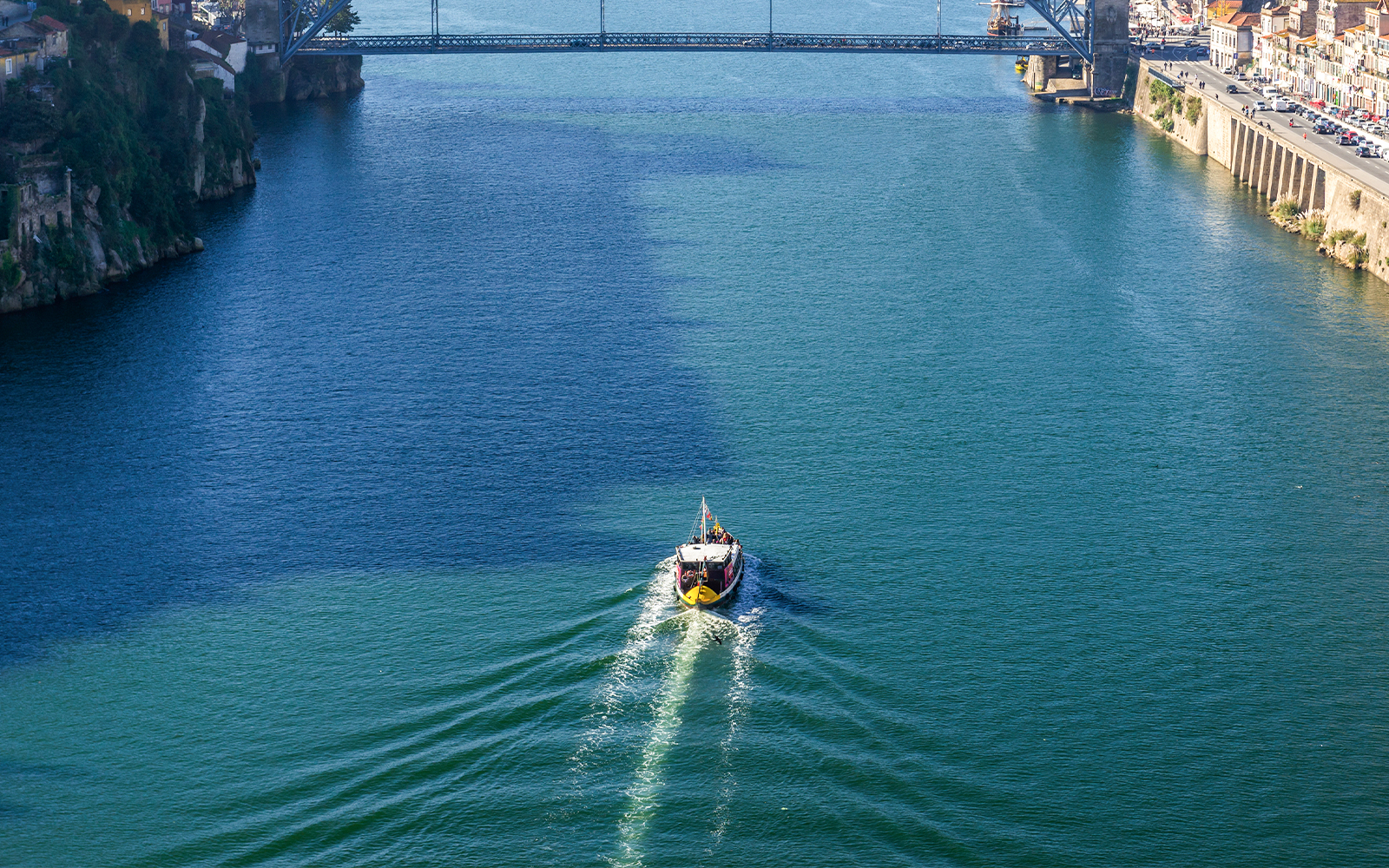 Boat cruising on the Douro River under a bridge in Porto, Portugal.