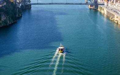 Boat cruising on the Douro River under a bridge in Porto, Portugal.