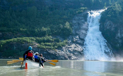 Canoe group paddling towards waterfall near Mendenhall Glacier, Alaska.