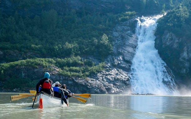 Canoe group paddling towards waterfall near Mendenhall Glacier, Alaska.